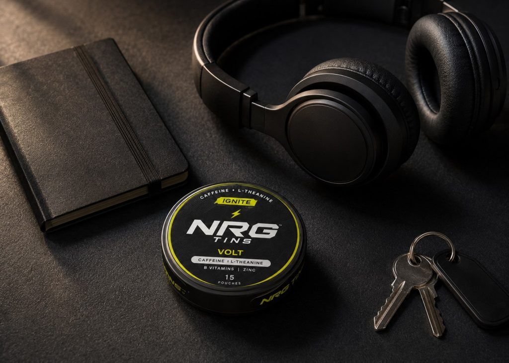 An NRG tin beside unbranded black headphones, a notebook and keys on a black desk.